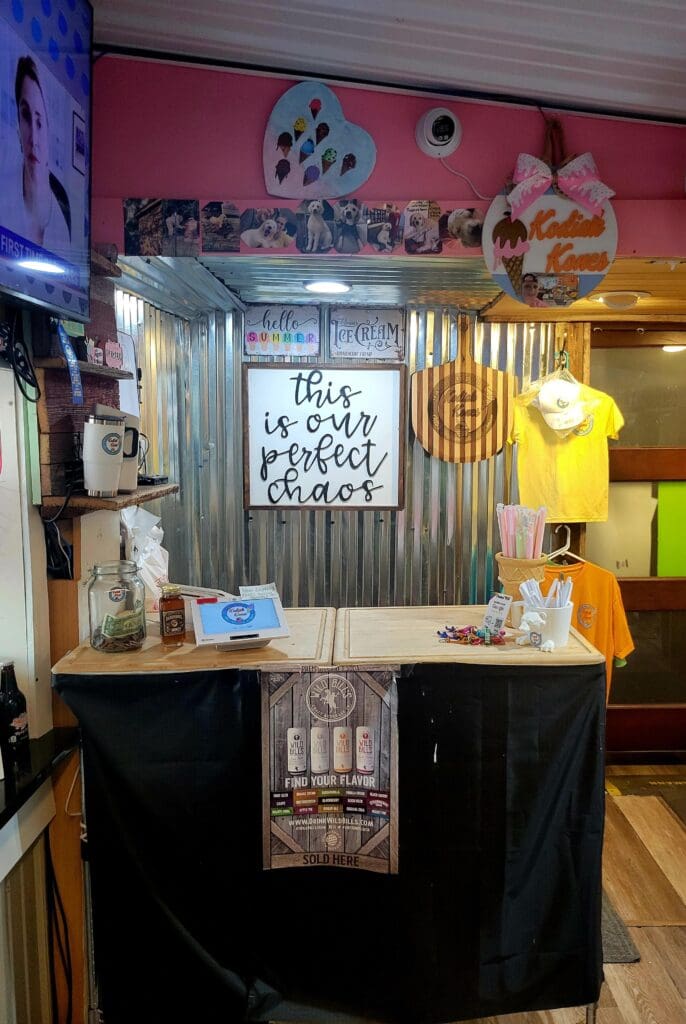 A retail vendor booth with a hot pink and black color scheme displays merchandise under yellow lighting at what appears to be an indoor event venue or fair.