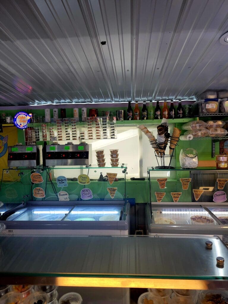 An indoor livestock exhibition display with bright green enclosure barriers, illuminated signage, and overhead industrial lighting in what appears to be a fair or agricultural venue.