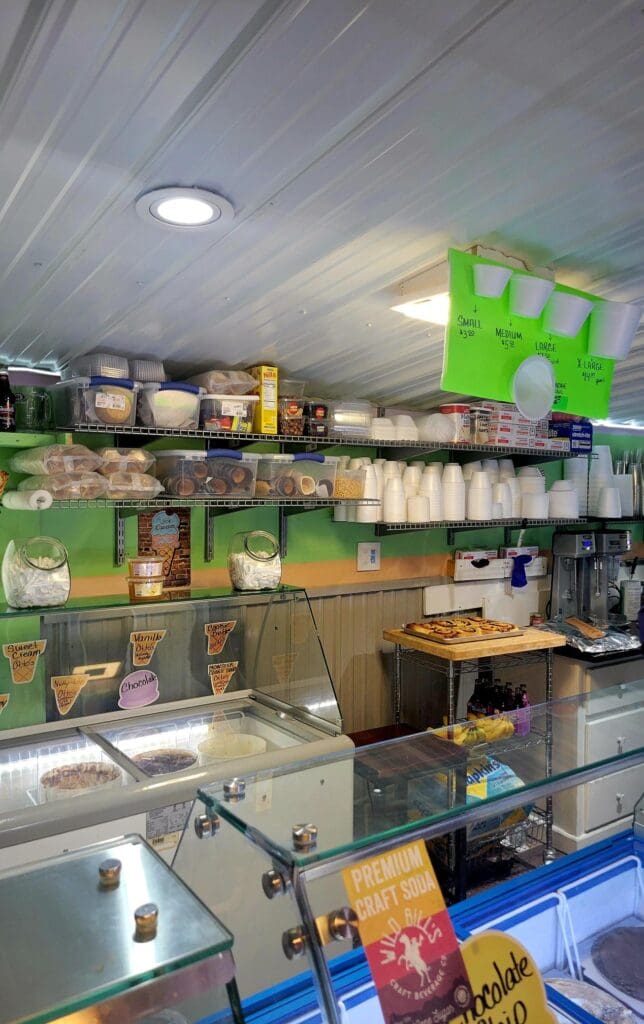 An organized workshop storage area with bright lime green shelving units stocked with various containers, boxes, and supplies under fluorescent ceiling lighting.