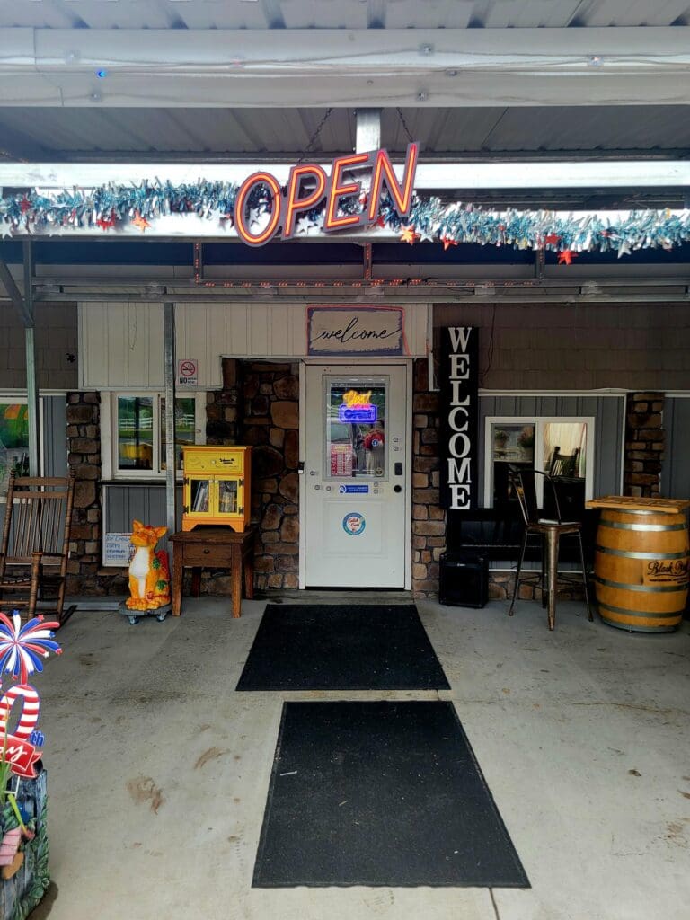 An empty food vendor stand with 'OPEN' signage sits beneath an overhead structure in what appears to be a parking lot or fairground venue during daytime.