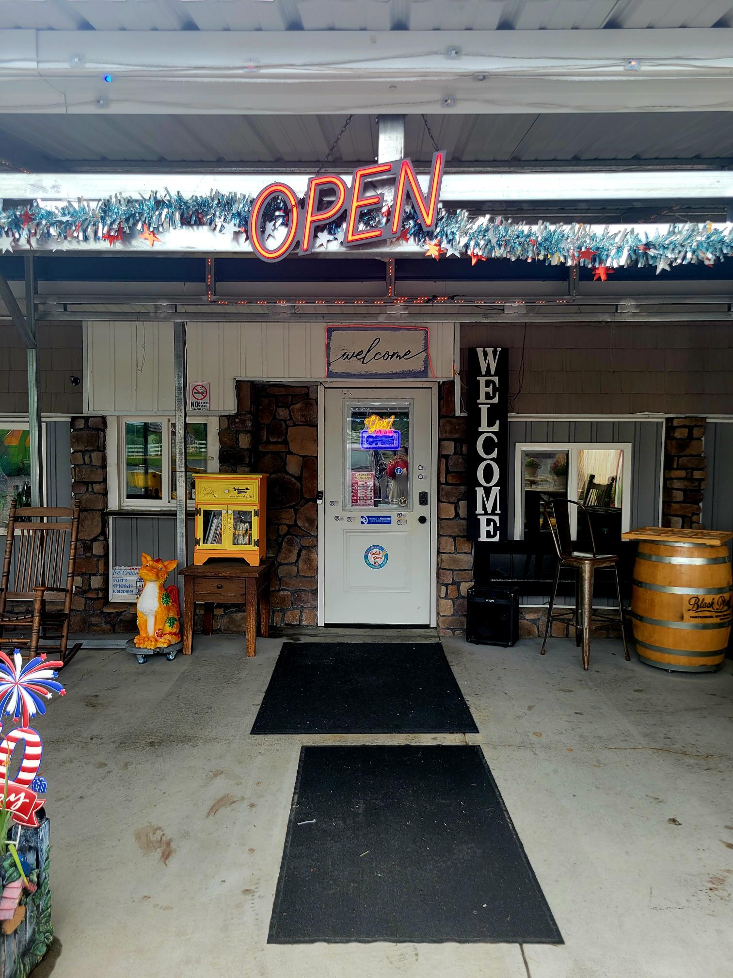 An empty food vendor stand with 'OPEN' signage sits beneath an overhead structure in what appears to be a parking lot or fairground venue during daytime.