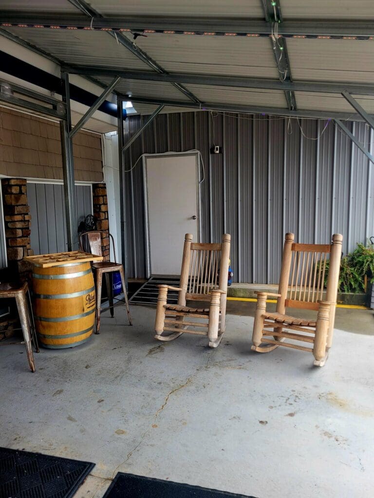 An interior view of a rustic workshop or storage space with corrugated metal walls, wooden chairs, and industrial storage elements.