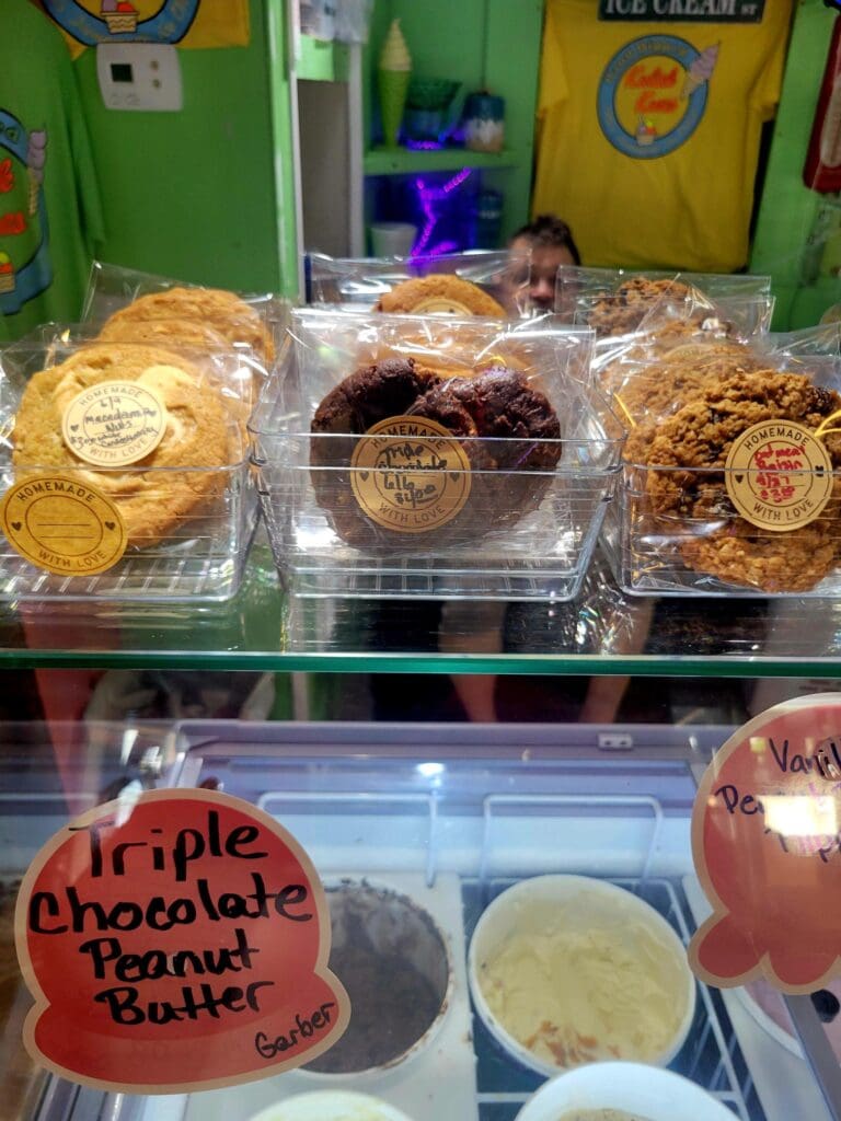 A display case showcases various baked goods and desserts including frosted pastries, chocolate items, and peanut butter treats at what appears to be a carnival or fair food stand.