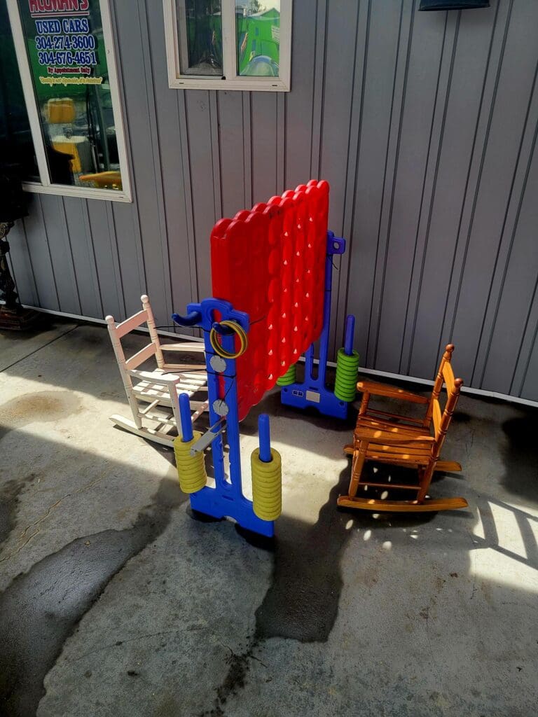 A red brick-laying machine sits in an outdoor workshop or industrial area next to a wooden chair and various tools.