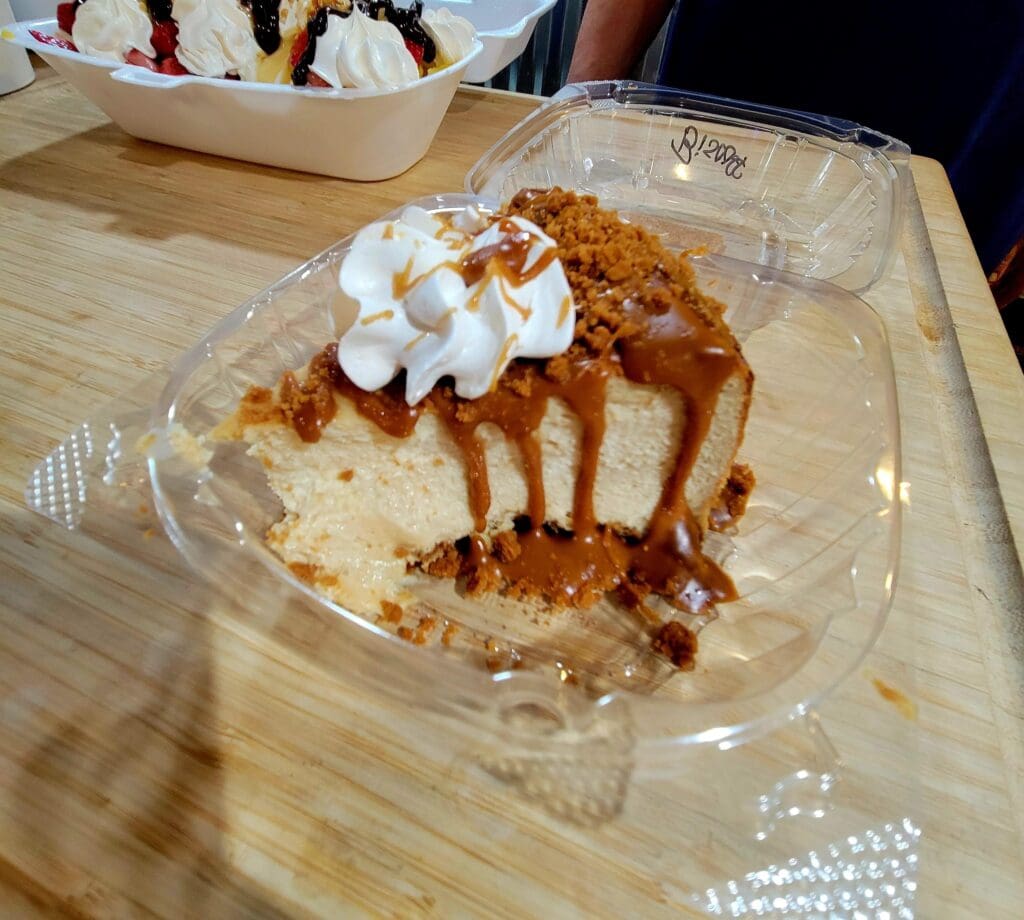 A caramel apple dessert topped with whipped cream and drizzled with caramel sauce sits on a clear plate atop a wooden surface.