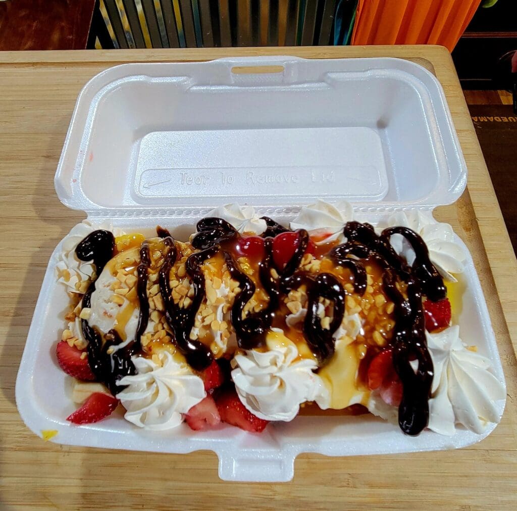 A gourmet crepe dessert topped with whipped cream, chocolate drizzle, and fresh berries served in a disposable food container.