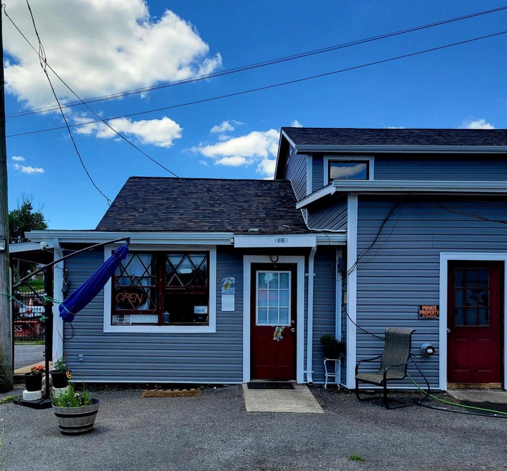 A small blue commercial building with a red door and storefront windows sits on a quiet street under a partly cloudy sky.