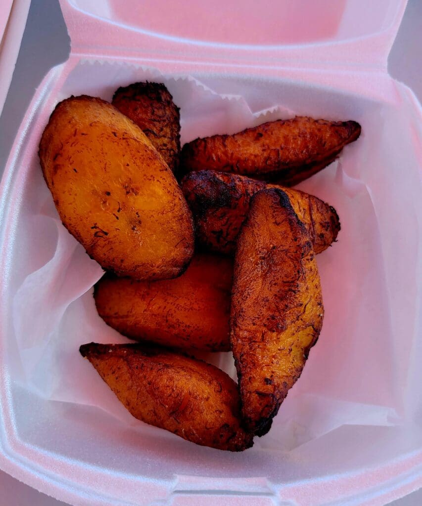 Crispy golden-brown fried plantains served in a pink disposable food container.