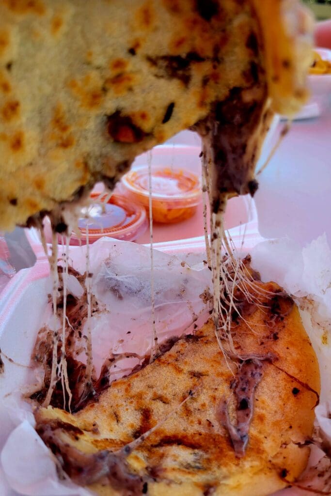 A close-up shot of a golden-brown fried food sandwich stacked on a plate with a beverage visible in the background.