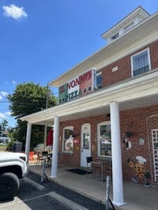 A charming brick storefront with white columns and covered porch in a quiet small town setting under clear blue sky.