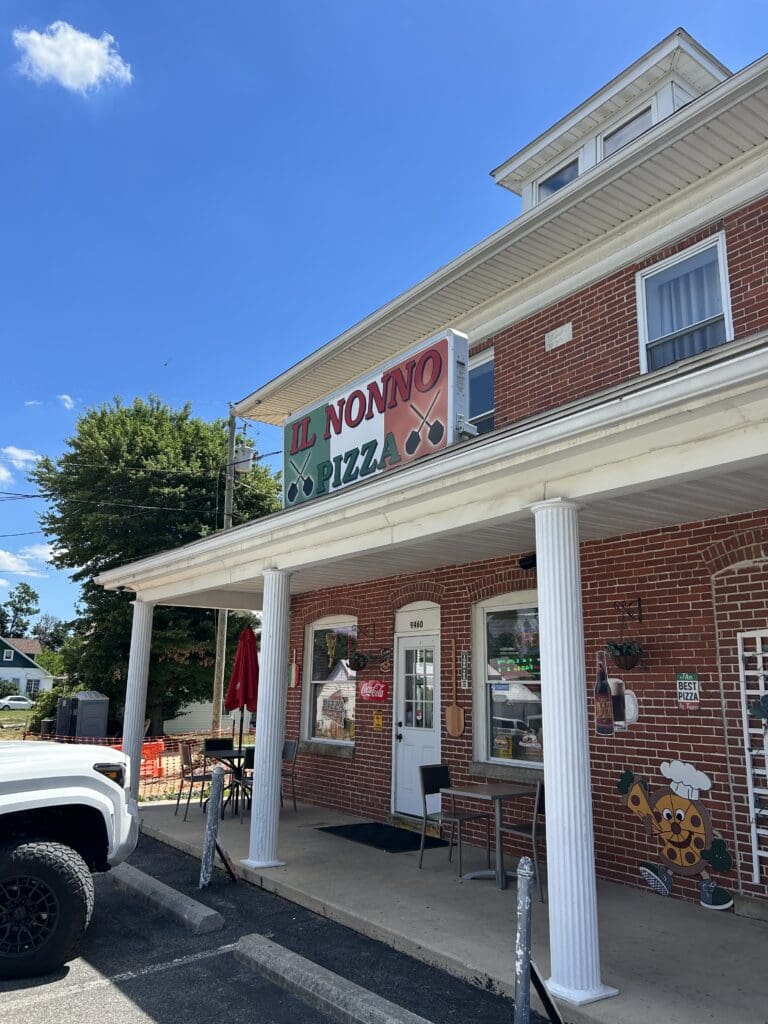A charming brick storefront with white columns and covered porch in a quiet small town setting under clear blue sky.