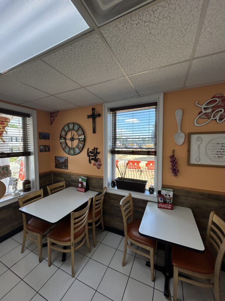 An empty casual dining room with warm orange walls, wooden furniture, and vintage-style decor including a large wall clock and decorative signage.