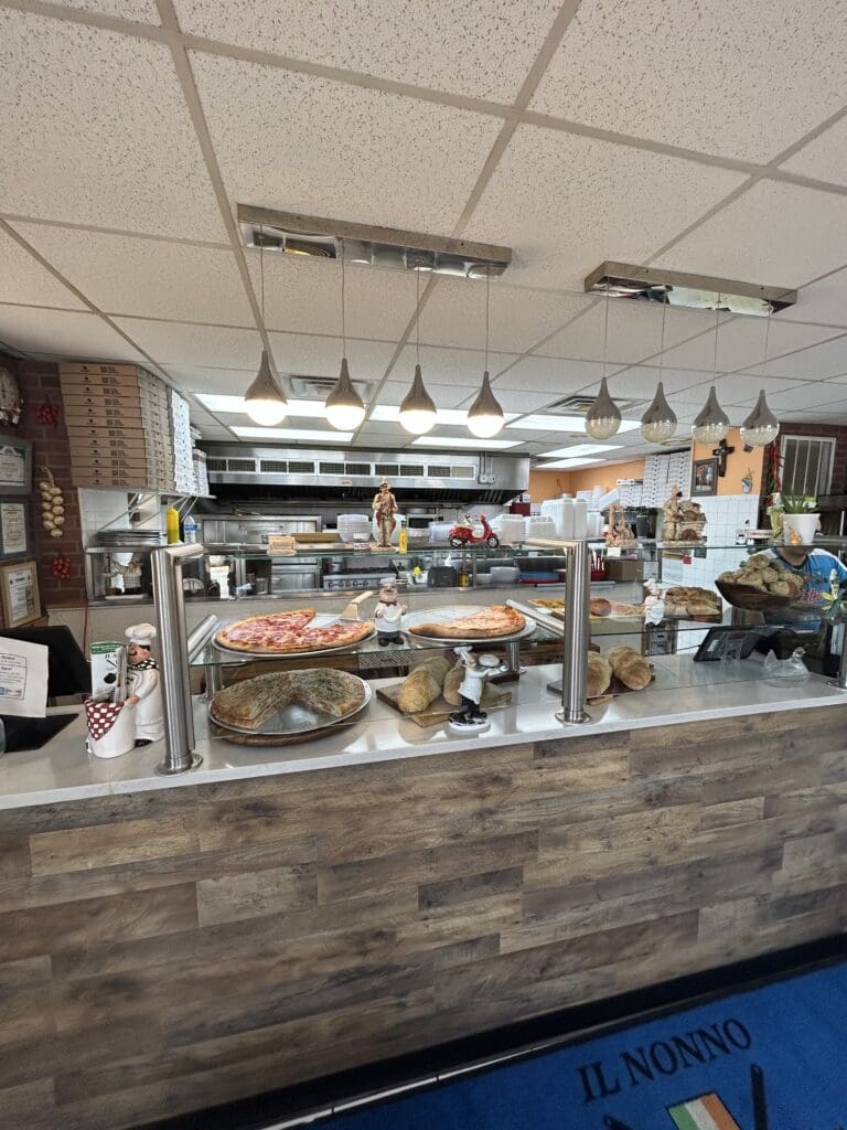 A modern food service counter with a wooden facade, glass display case, and pendant lighting in what appears to be a commercial kitchen or restaurant setting.