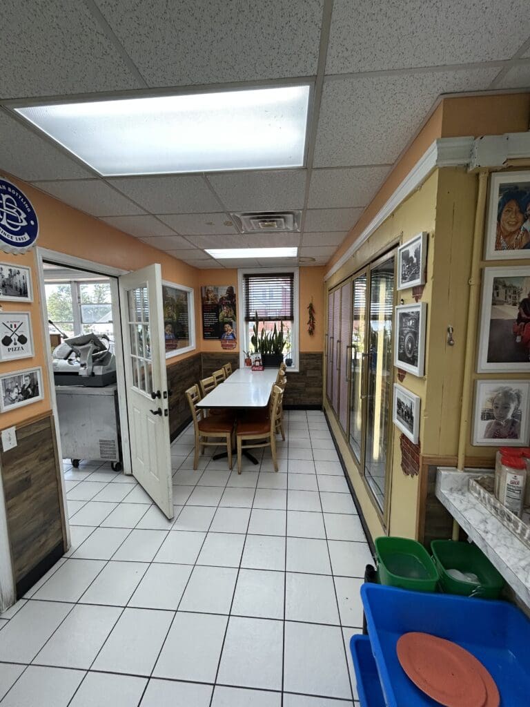 An institutional workshop or break room with a work table, appliances, and bulletin boards on the walls under fluorescent lighting.