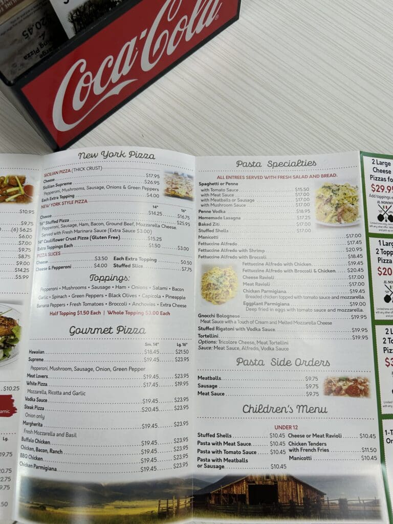 An overhead view of an open restaurant menu with a Coca-Cola sign and condiment bottles visible on the table.