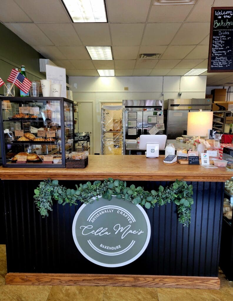 A cozy coffee shop counter with a neon circular sign, pastry display, and organized workspace behind the service counter.