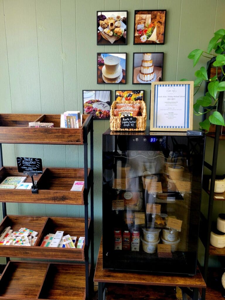 A cozy retail or cafรฉ display featuring shelved coffee products, framed artwork on the wall, and a glass-front cabinet showcasing various items in warm wooden surroundings.