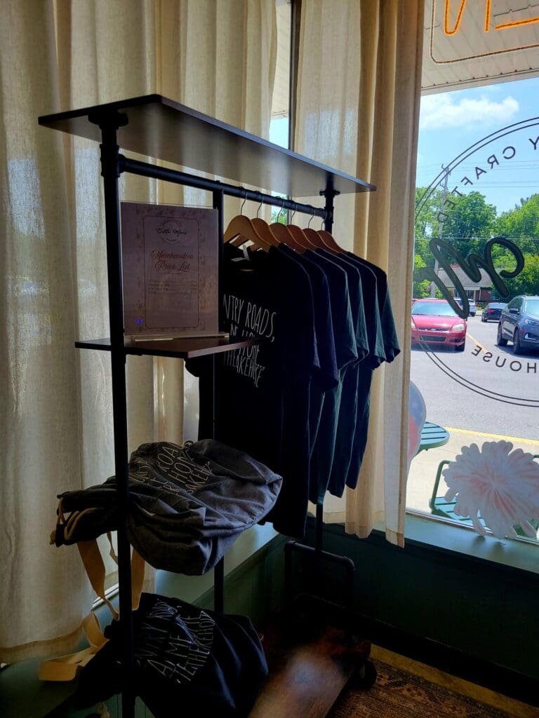 An indoor scene showing a black clothing rack with dark garments hung on it, positioned in front of a window and television in what appears to be a residential space.