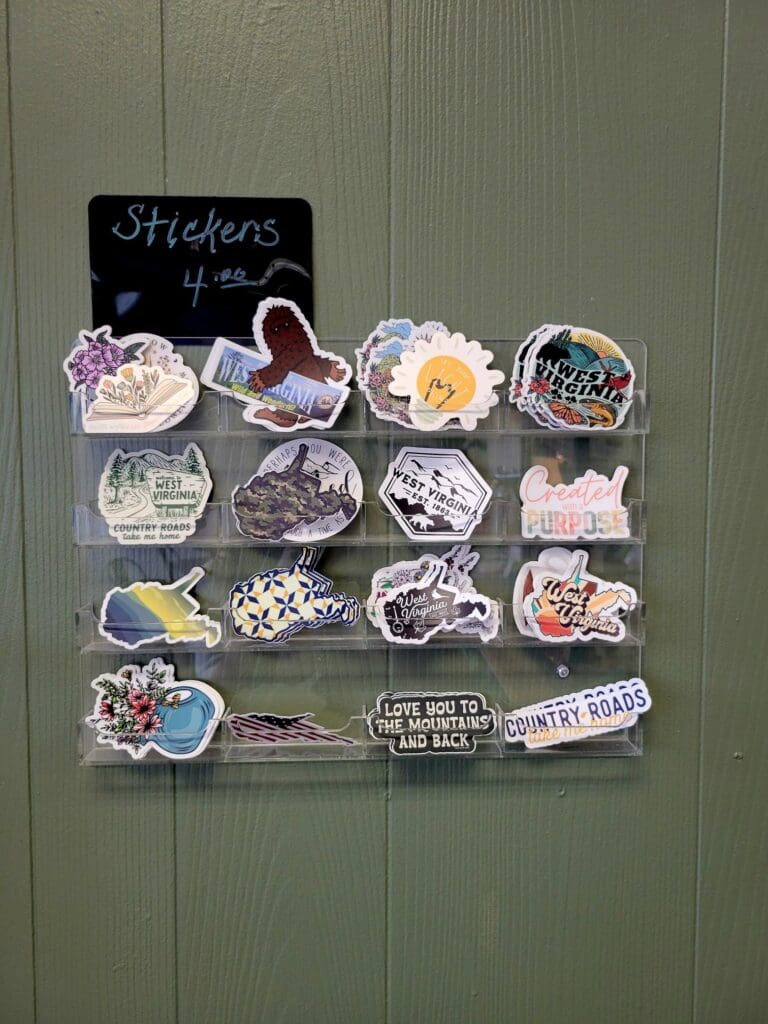 A collection of colorful decorative stickers arranged on a display board mounted on a sage green wooden wall, with a chalkboard sign reading 'Stickers' at the top.