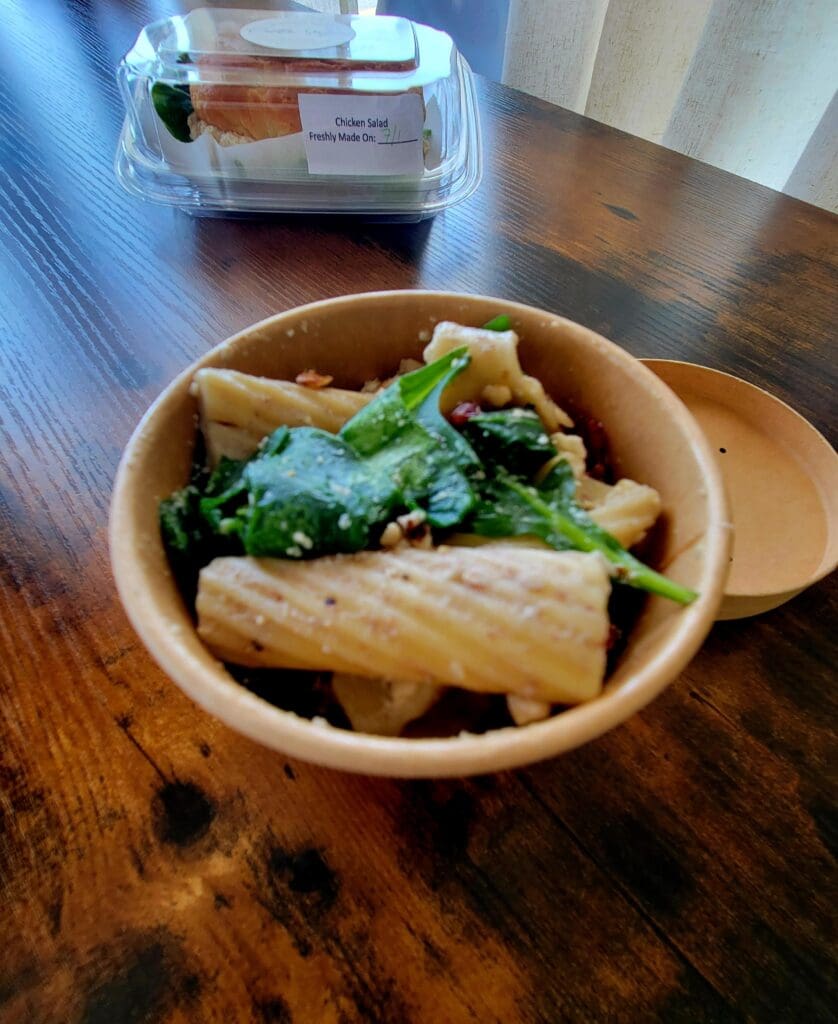 A bowl of Asian noodles with greens served in a rustic wooden bowl on a dark wood table.