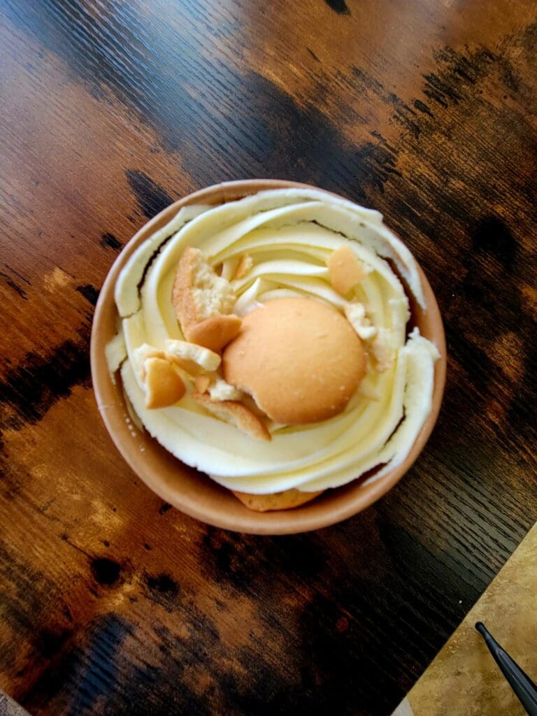 A creamy hummus dip topped with a whole chickpea and olive oil served in a white ceramic bowl on a rustic wooden table.