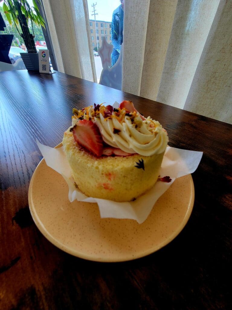 A gourmet pastry topped with fruit compote and garnish sits on a wooden plate in an indoor dining setting.