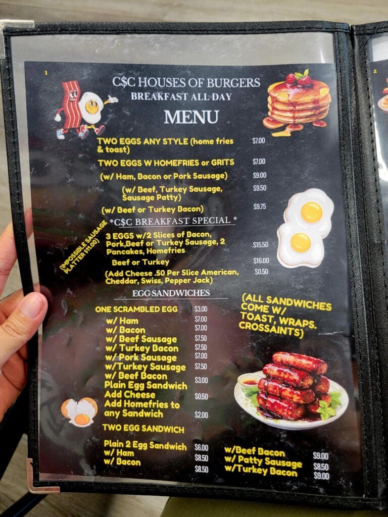 A person holds open a dark-themed restaurant menu displaying burger and breakfast items with food photography.