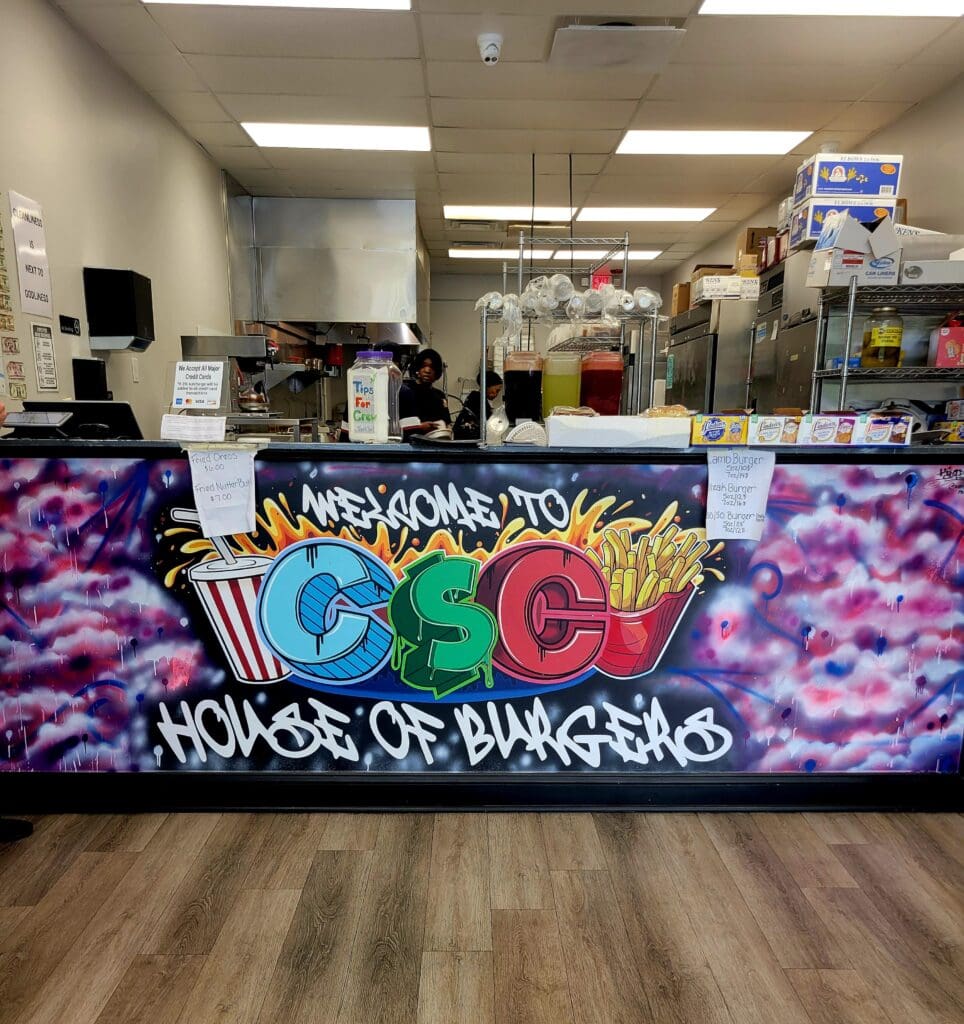 A colorful graffiti-style mural decorates the counter of an indoor retail shop with vibrant pink, purple, blue, and green lettering and artwork.