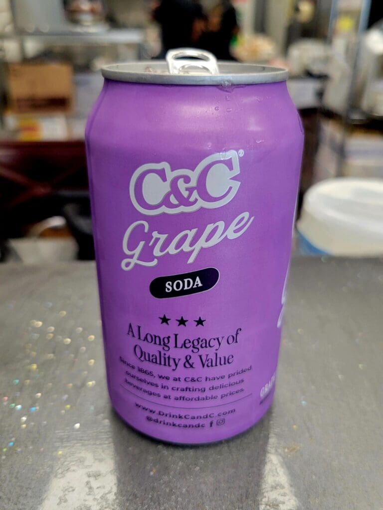 A purple C&C Grape soda can sits on a kitchen counter with a blurred domestic background.