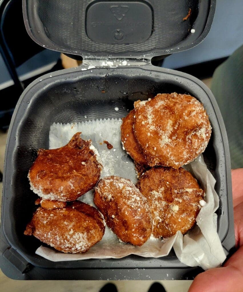 Freshly fried golden-brown chicken patties arranged in an open styrofoam takeout container lined with parchment paper.