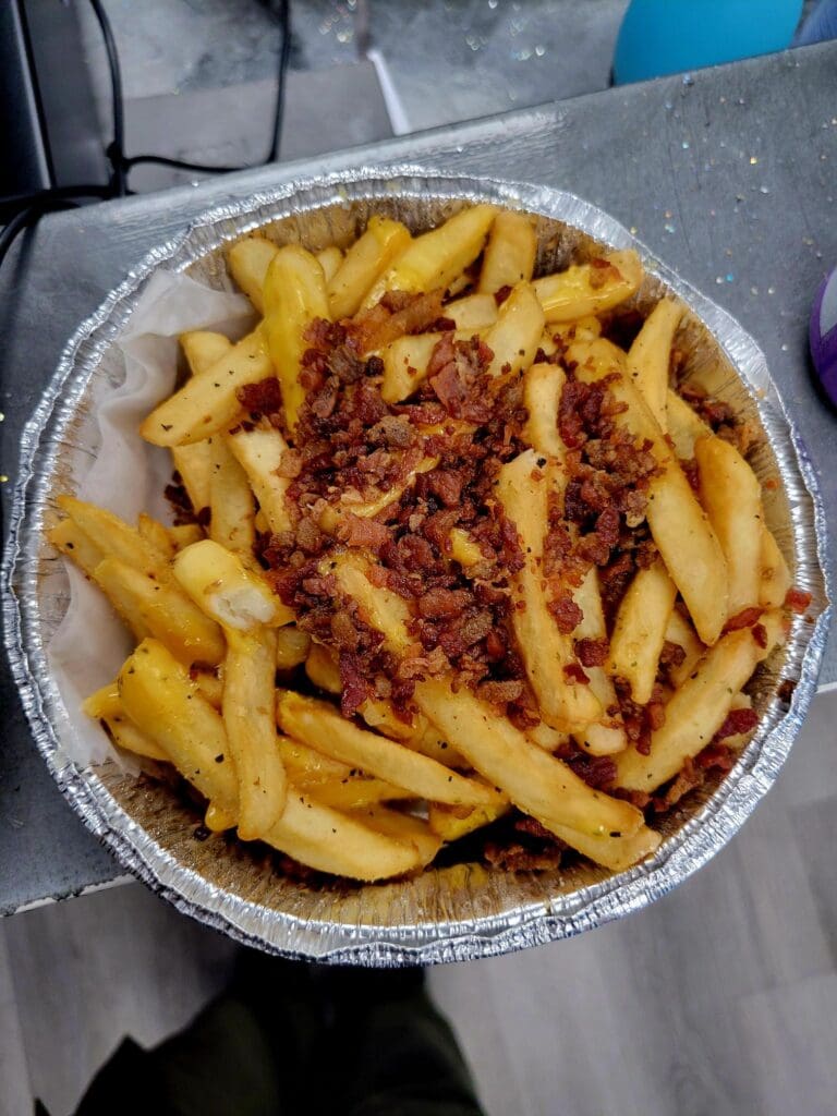 A serving of golden French fries topped with red seasoning served in a disposable aluminum container.