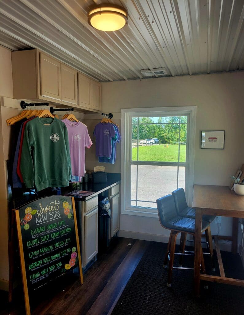 A bright workshop or studio space with a clothing rack, workbench, and organized storage, featuring natural light from a glass door and window.
