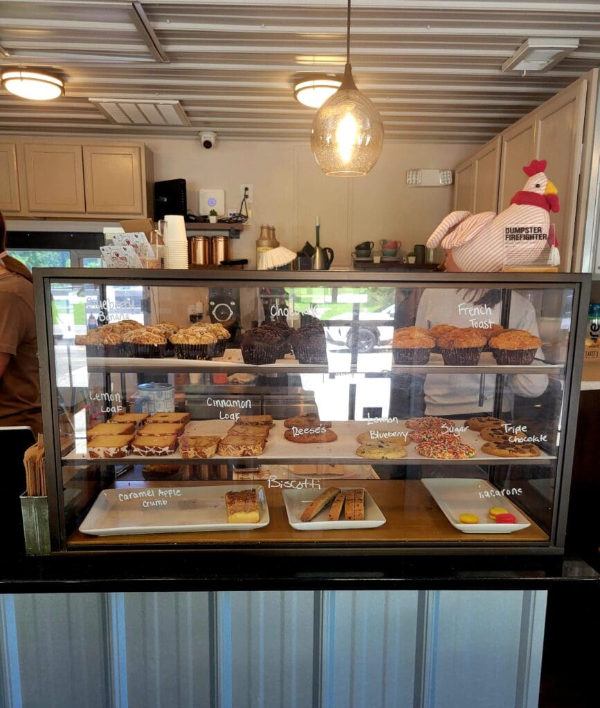 A well-lit bakery display case showcases various fresh baked goods including bread, pastries, and other items in a rustic wooden storefront setting.