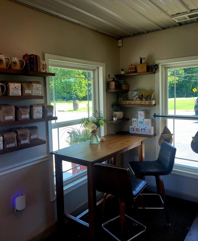 A bright, organized home office workspace with wooden desk, shelving units, and large windows overlooking greenery.