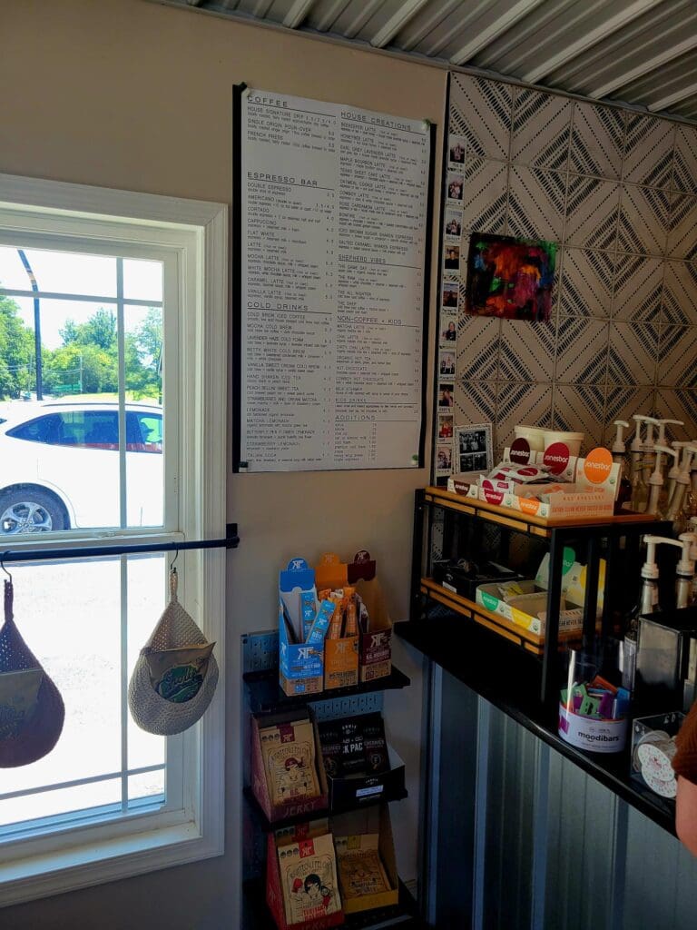 A personal home workspace or study nook with a desk, shelving, bulletin board, and large window showing an outdoor view, decorated with patterned wallpaper.
