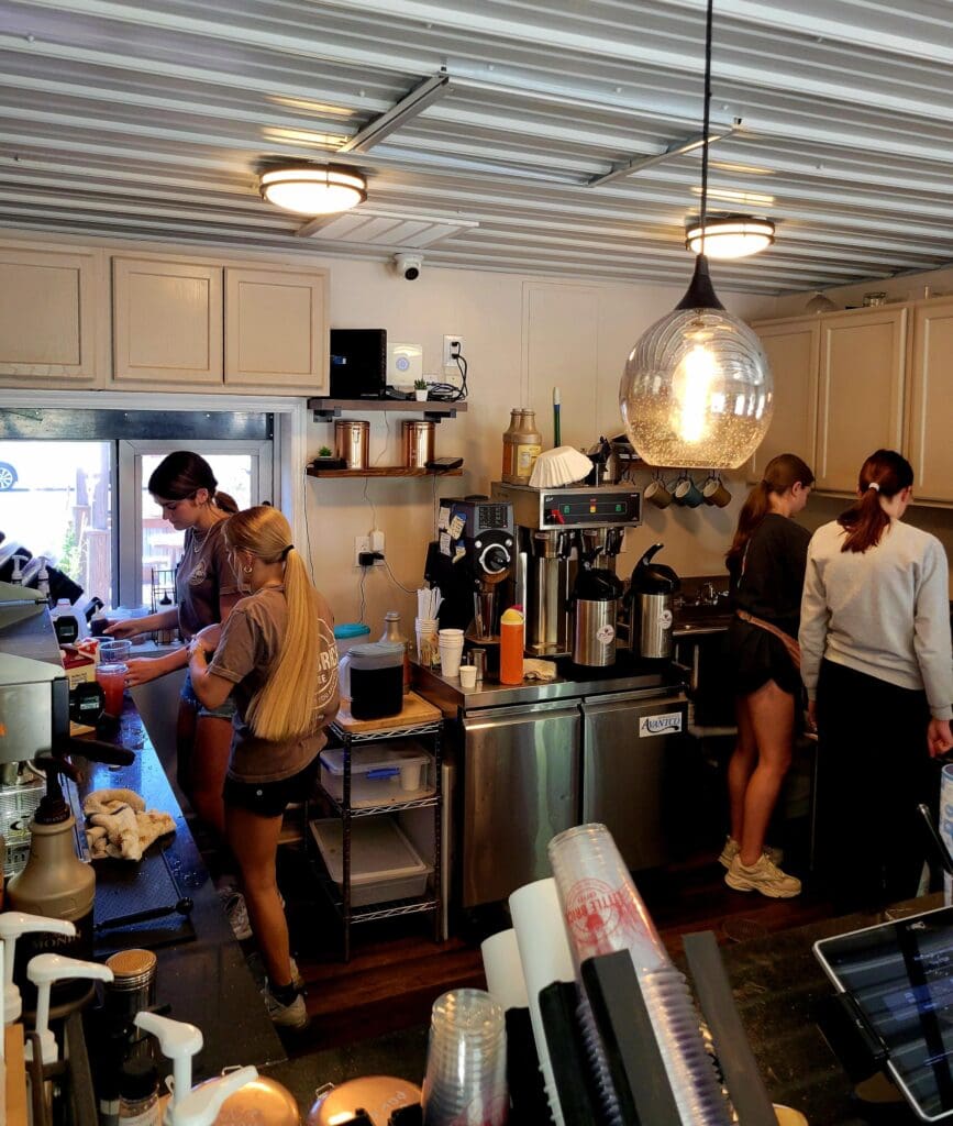 A group of participants engaged in a culinary workshop or cooking class in a professional kitchen space with multiple people gathered around counters and equipment.