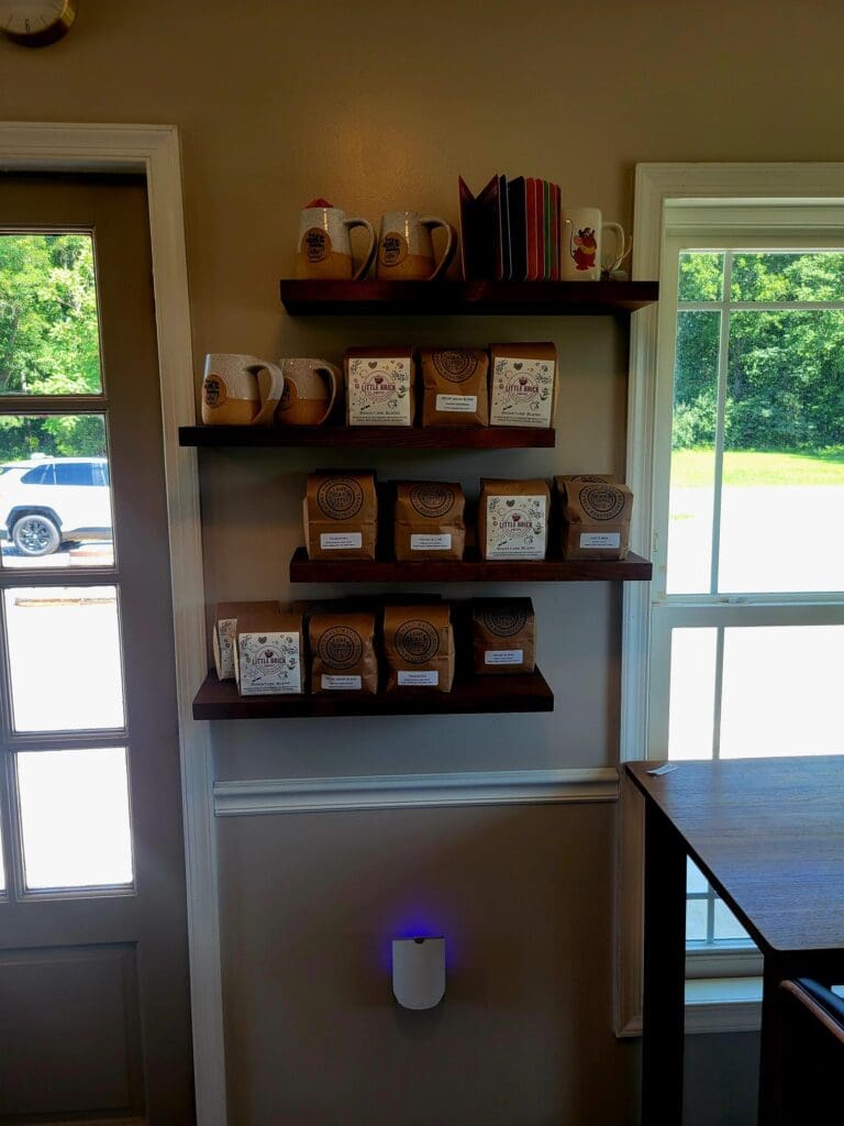 An organized retail display with shelving mounted above glass doors, featuring packaged coffee products, decorative items, and a small diffuser on the counter.