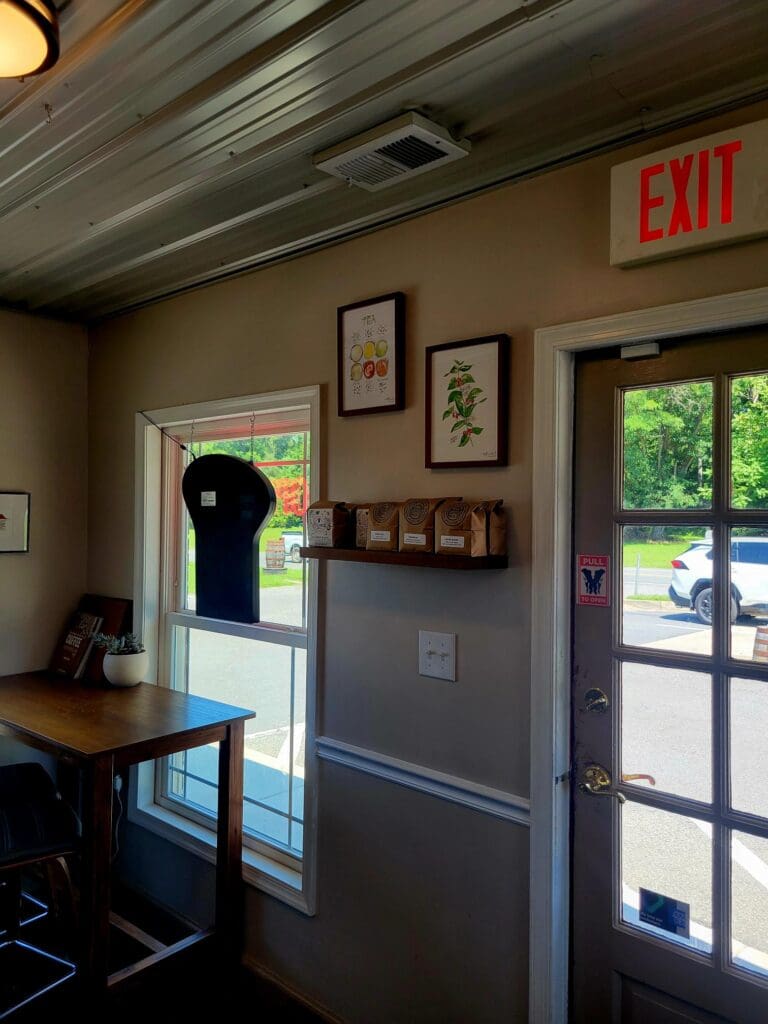 An interior view of a workshop or utility room with a workbench, refrigerator, exit sign, and glass doors leading outside.