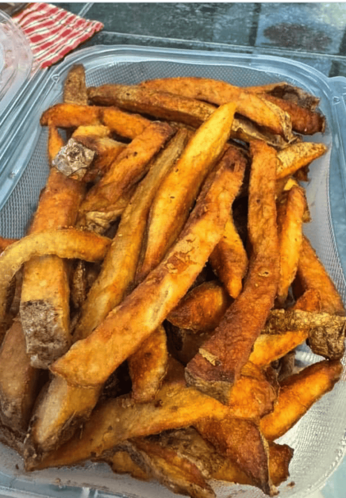A close-up overhead view of golden-brown sweet potato fries in a clear plastic container with an American flag visible in the background.