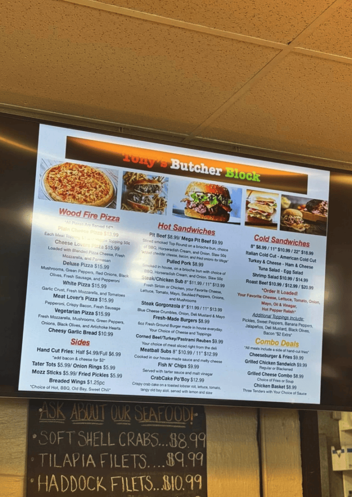 A digital menu board displaying food items with orange branding and multiple food photographs mounted on an indoor ceiling.