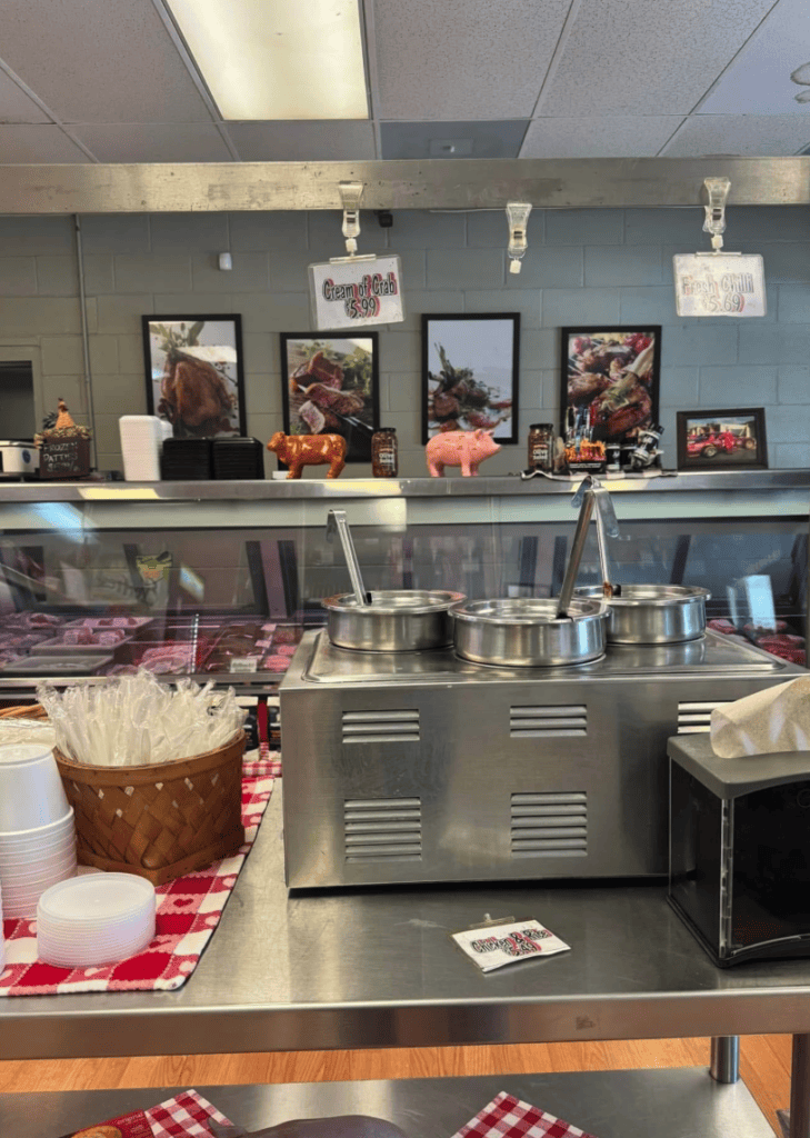 A professional food service kitchen with stainless steel equipment, decorative backdrop, and red checkered table linens in a well-lit establishment.