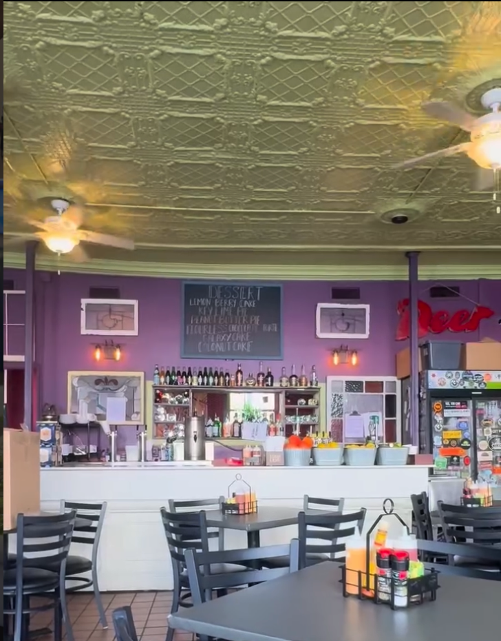 An empty beauty salon interior with purple walls, decorative ceiling tiles, styling stations with mirrors, and retail product displays.