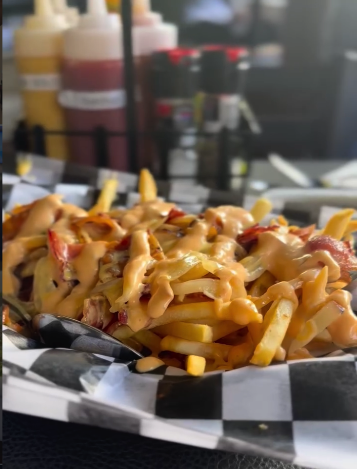 A close-up shot of golden waffle fries served in a checkered paper container at what appears to be a food carnival or street vendor stand.