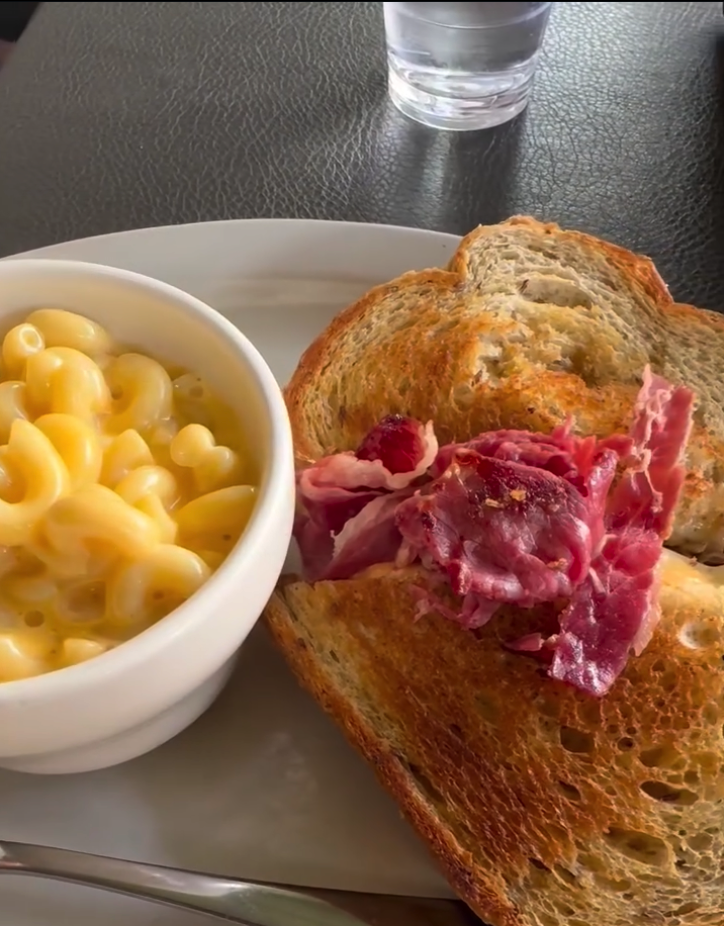 A plate of mac and cheese alongside toasted bread topped with cured meat, served at an indoor dining venue.