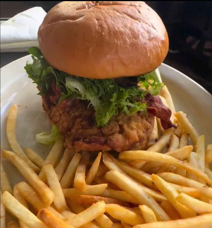 A golden fried chicken burger topped with fresh lettuce served on a white plate alongside a generous portion of crispy french fries.