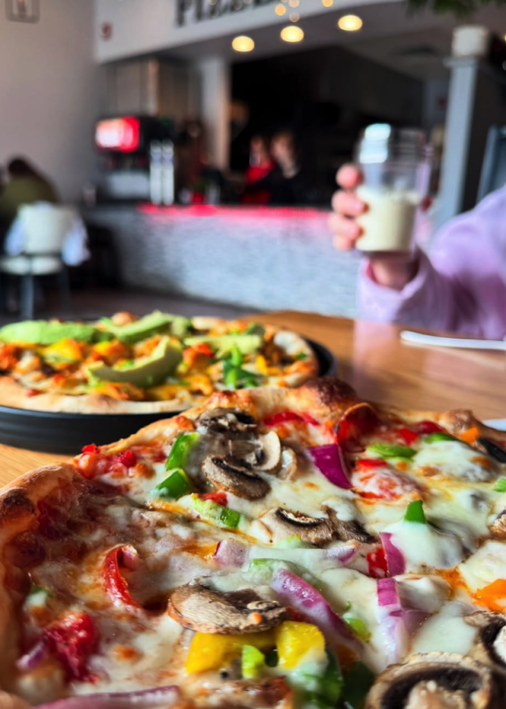 A close-up of freshly prepared pizzas with colorful toppings displayed at a busy food venue or pizzeria counter.
