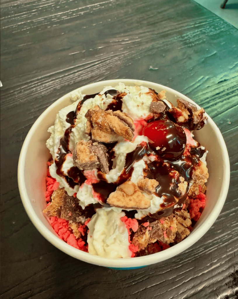 An overhead view of a bowl of vanilla ice cream topped with fresh berries and whipped cream served on a wooden table.