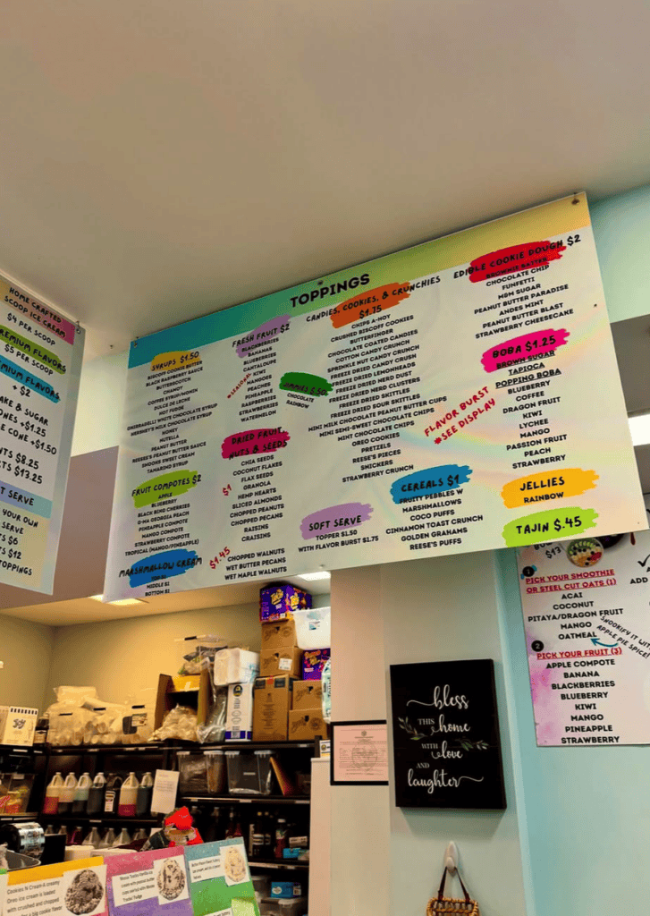 A classroom wall displays colorful educational posters and bulletin boards with various subjects and information, along with shelving and storage below.