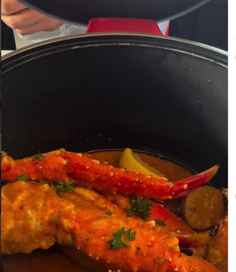 A freshly cooked lobster with garnish sits in a black pot with a red lid, captured in close-up detail.