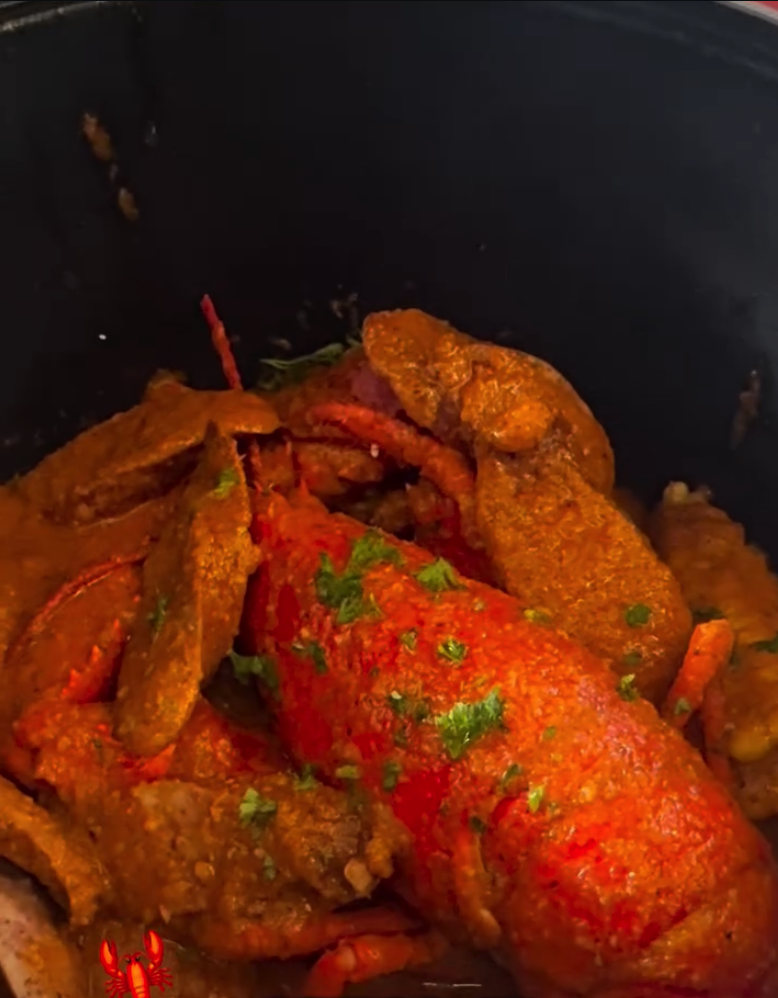 A close-up of seasoned poultry pieces cooking in a dark pot with red peppers and aromatic spices.